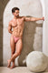 Fit male model in pink bikini underwear posing in minimal indoor setting with stone decor
