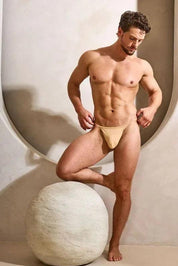 Athletic man modeling beige men's thong underwear in a modern, minimal studio setting.