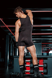 Man in black sleeveless bodysuit and gloves posing in gym with dumbbells and red lighting.