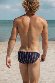 Man in striped swim briefs on beach, showcasing men's sexy swimwear for summer fashion
