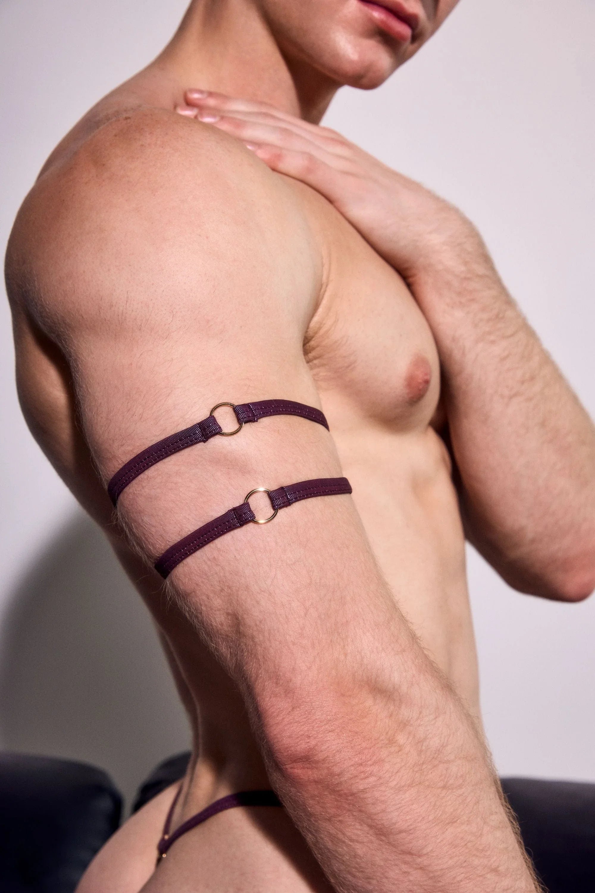 Shirtless male model wearing purple double arm harness straps and matching underwear