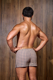 Shirtless man modeling plaid men’s boxer shorts against a wood panel background