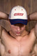 Shirtless man wearing a mesh trucker cap with 'COYOTE' text, posing arms behind head