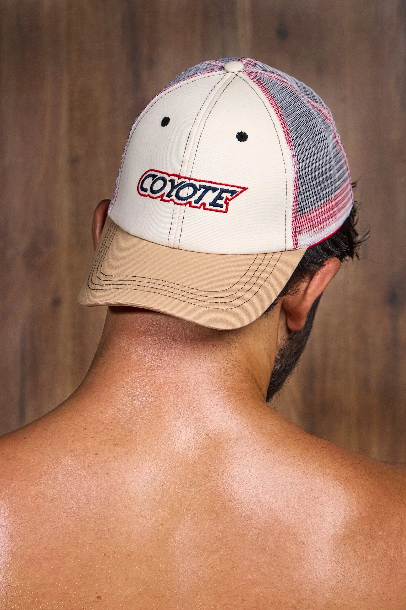 Man wearing a beige and mesh trucker hat with 'COYOTE' text, wooden background