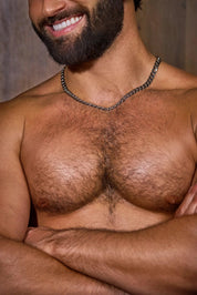 Shirtless bearded man with hairy chest and chain necklace, arms crossed, smiling