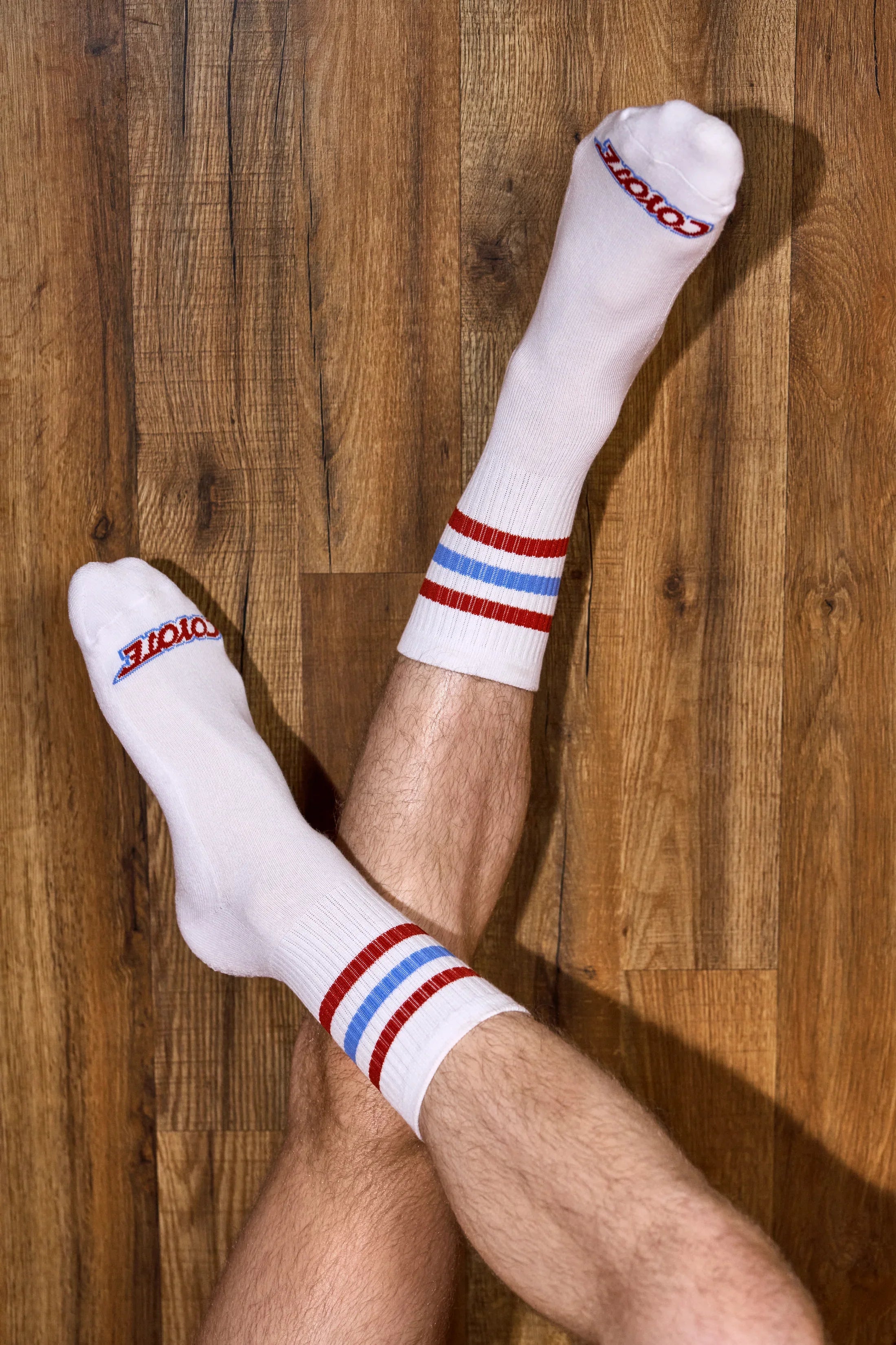 White athletic socks with red and blue stripes worn on crossed legs on wood floor