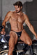 Shirtless man in black leather thong underwear sitting on a motorcycle against a concrete wall