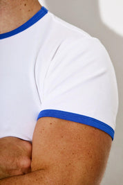 Close-up of a man's arm wearing a fitted white t-shirt with blue trim on sleeve and collar