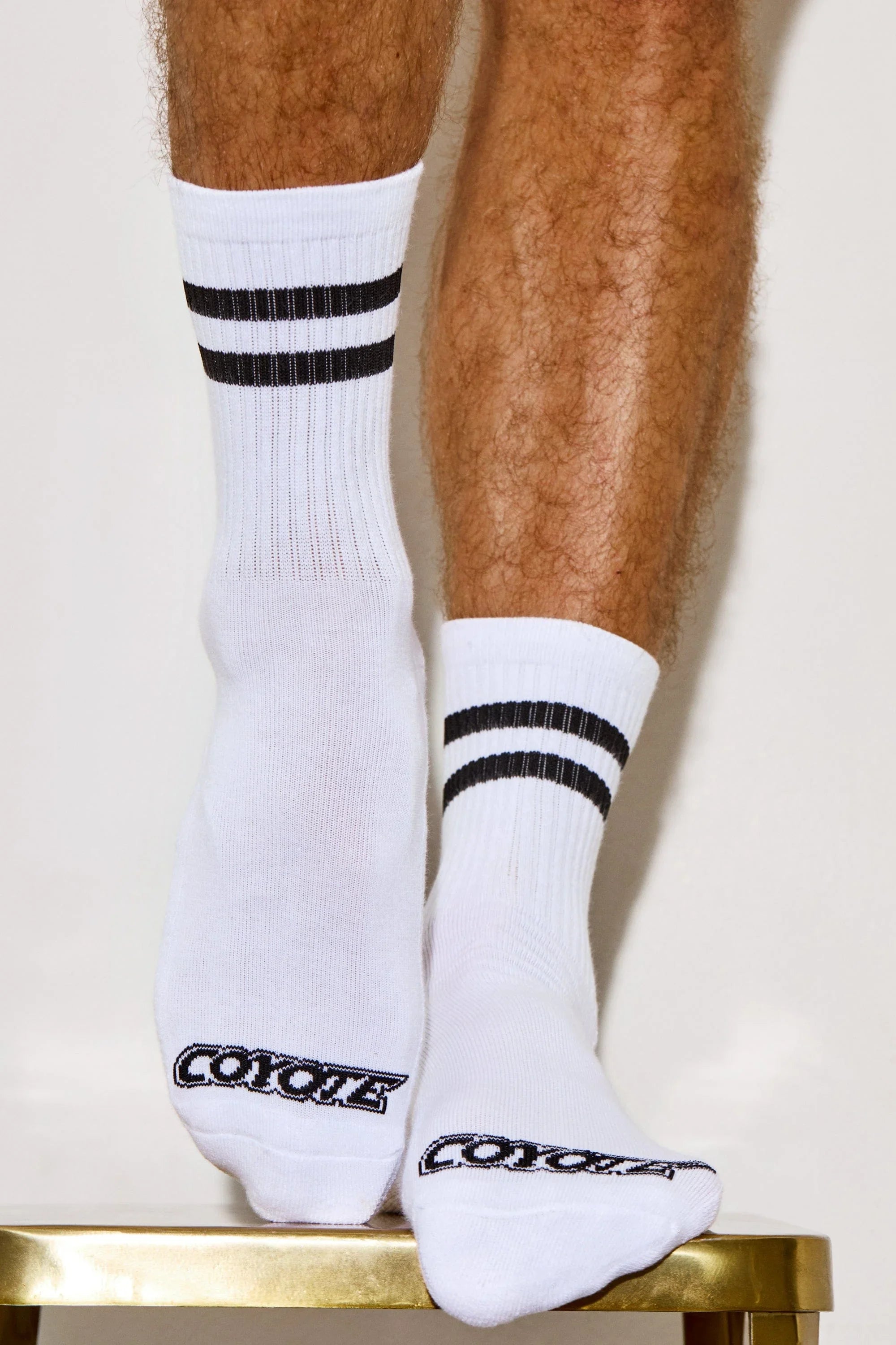 White athletic socks with black stripes and Coyote text, worn on hairy male legs