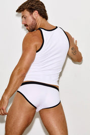 Man in white tank top and white briefs with black trim posing against a plain wall