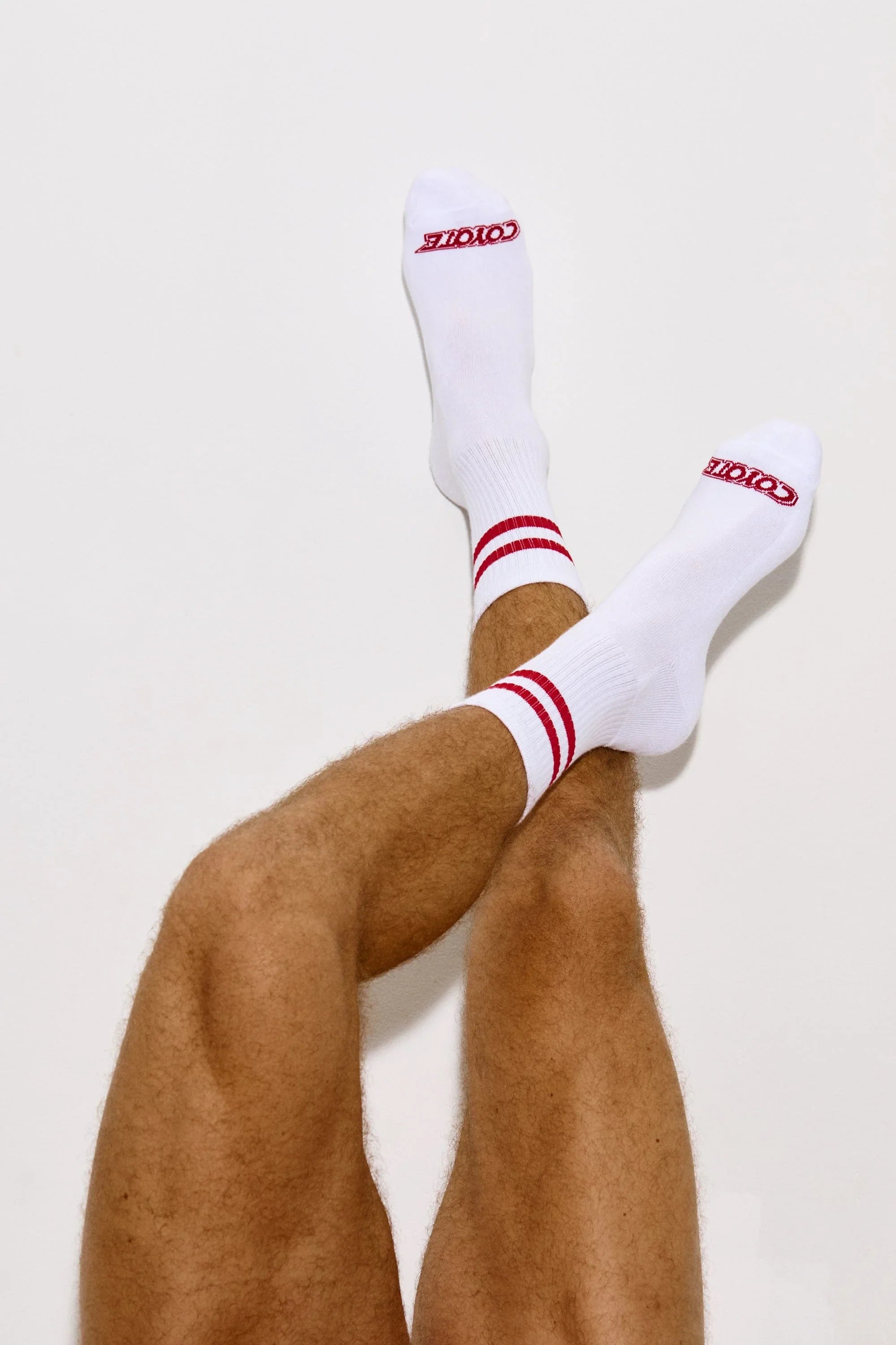 Man's legs crossed wearing white athletic socks with red stripes and logo on toes