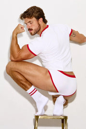 Man posing in white and red trim underwear set, flexing arm, wearing athletic socks.
