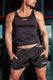Athletic man in black mesh shorts and tank top, gym locker room background, sporty underwear waistband showing