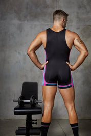 Man in sporty black singlet with pink and blue stripes stands by gym bench and dumbbell