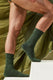Man in green socks and underwear stepping up white stairs with olive fabric backdrop