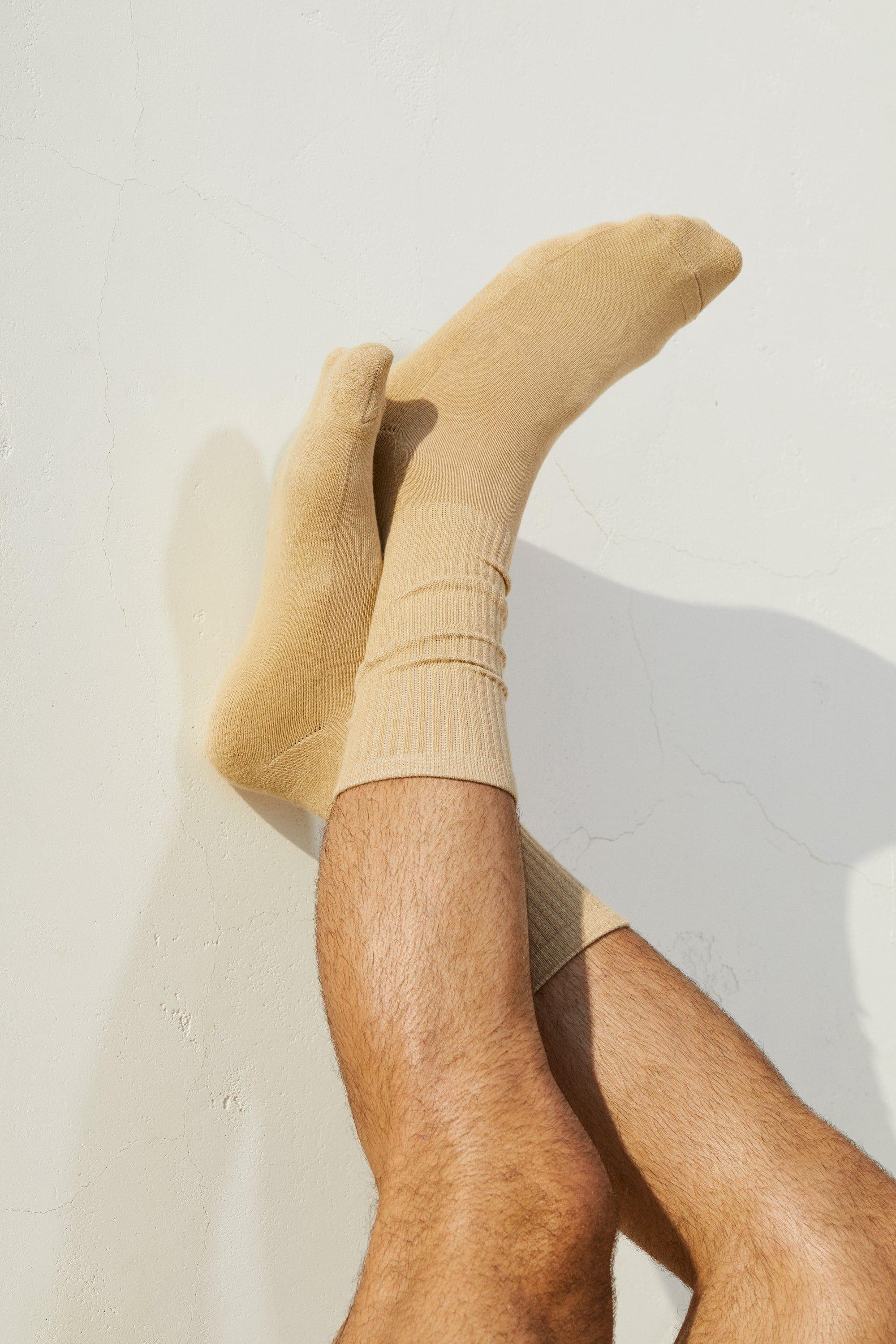 Man's legs crossed wearing beige socks against a light wall, men's fashion socks