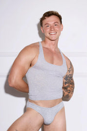 Man in gray athletic tank top and matching men's underwear, showcasing fit physique against white wall