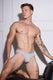 Muscular man in gray men's underwear posing against white paneled wall, showcasing fit physique and tattoos