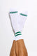 White crew socks with green stripes and logo on toes, worn on crossed legs against white background.