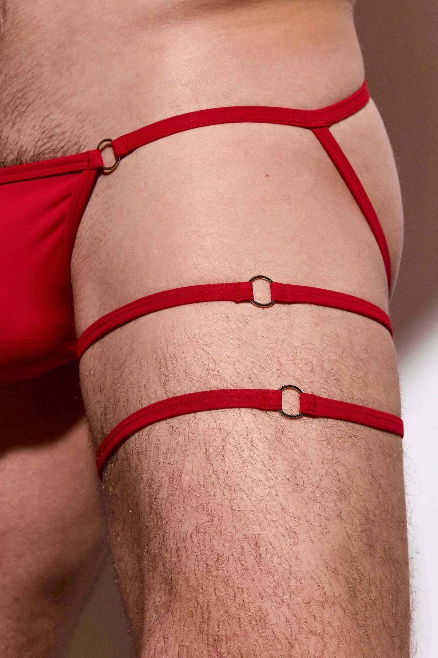 Close-up of male thigh wearing red strappy underwear with ring detailing, sexy men's lingerie