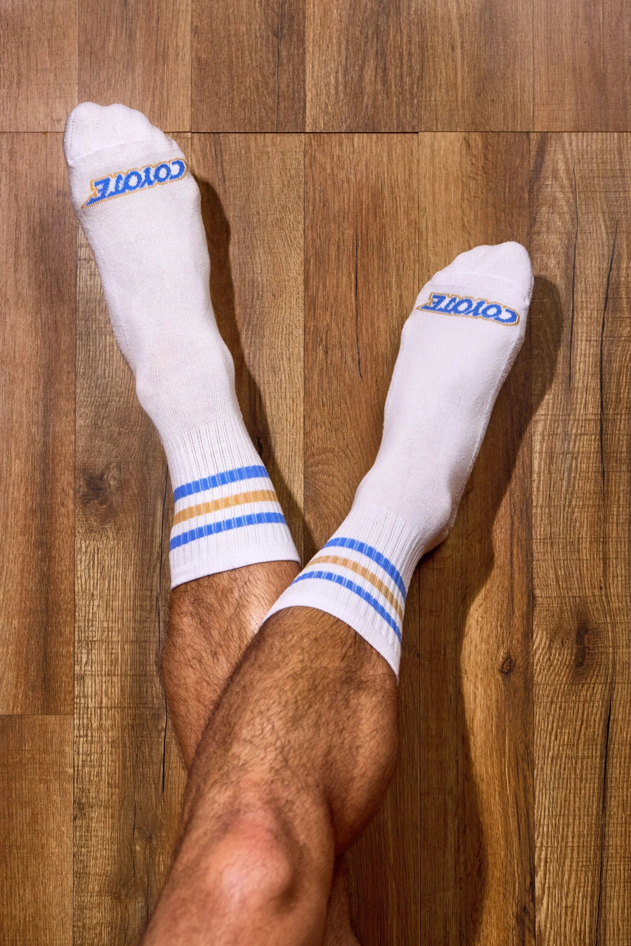 White athletic socks with blue and gold stripes worn on crossed legs on wood floor