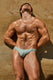Muscular man modeling light blue men's bikini underwear against a sandy rock wall