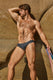 Muscular man modeling grey men's swim brief against rocky outdoor background