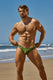Muscular man wearing green swim briefs on sandy beach, blue sky and ocean in background
