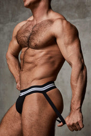 Muscular man modeling black jockstrap underwear with striped waistband against gray background